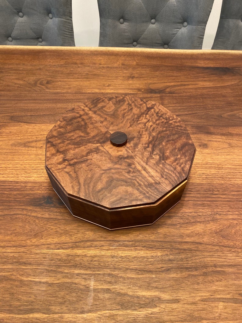 May include: A wooden octagonal box with a dark brown finish and a small wooden knob on the lid.