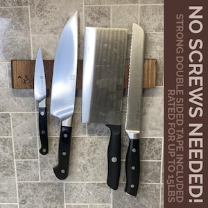 May include: A wooden magnetic knife holder with four knives attached. The holder is made of dark wood and has a natural finish. The knives are all different sizes and shapes, and they are all made of metal. The holder is labeled "NO SCREWS NEEDED! STRONG DOUBLE SIDED TAPE INCLUDED RATED FOR UP TO 15 LBS".