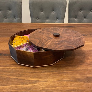 May include: A wooden octagonal box with a lid. The box is made of dark wood with a light wood inlay. The lid has a small knob on top. The box is filled with small, colorful items.