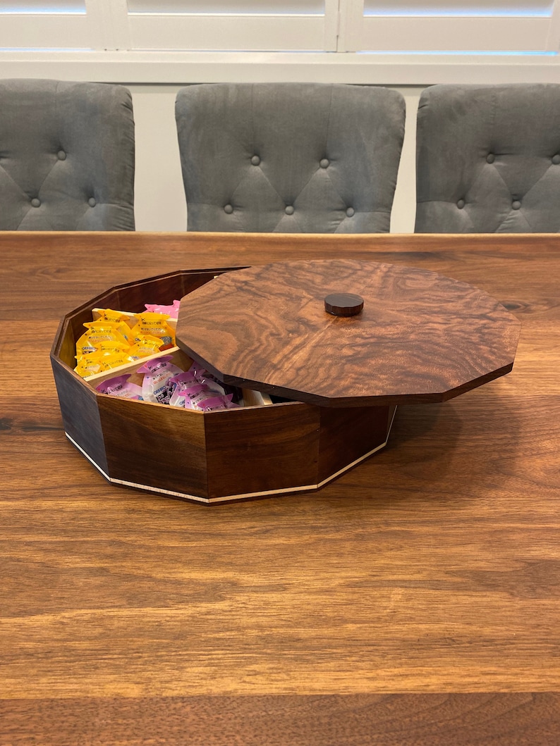 May include: A wooden octagonal box with a lid. The box is made of dark wood with a light wood inlay. The lid has a small knob on top. The box is filled with small, colorful items.