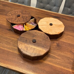 May include: Three wooden octagonal boxes with lids. The boxes are made of different types of wood, one is a light wood with a natural finish, the other two are a darker wood with a rich brown finish. The boxes are arranged on a wooden table.