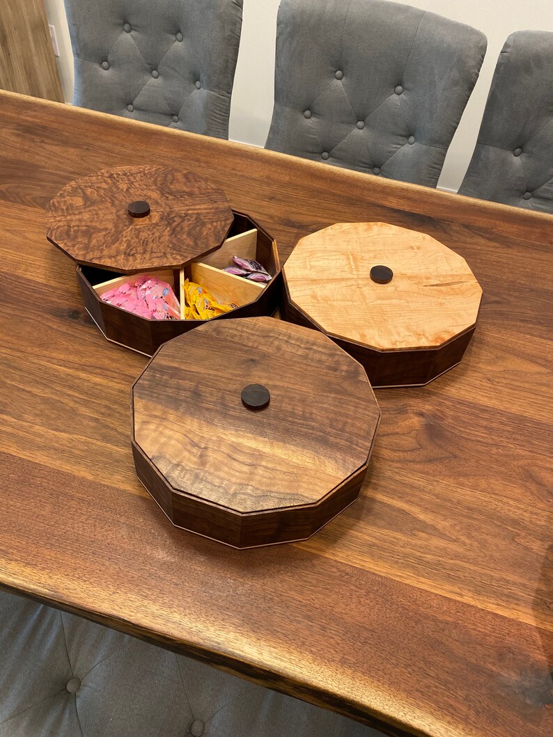May include: Three wooden octagonal boxes with lids. The boxes are made of different types of wood, one is a light wood with a natural finish, the other two are a darker wood with a rich brown finish. The boxes are arranged on a wooden table.