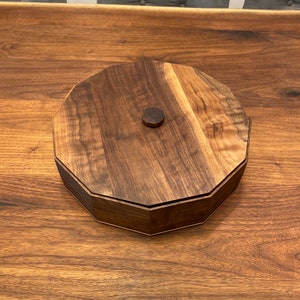May include: A round wooden box with a lid, made of dark walnut wood. The lid has a small, round knob in the center.