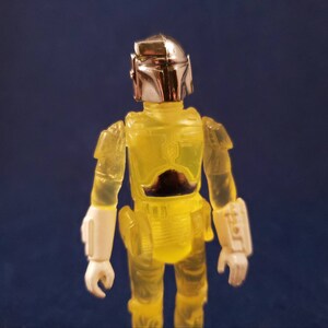 May include: A yellow translucent action figure of a bounty hunter with a silver helmet and white gauntlets.