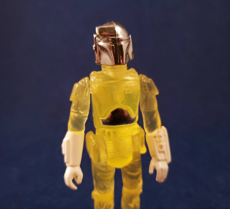 May include: A yellow translucent action figure of a bounty hunter with a silver helmet and white gauntlets.