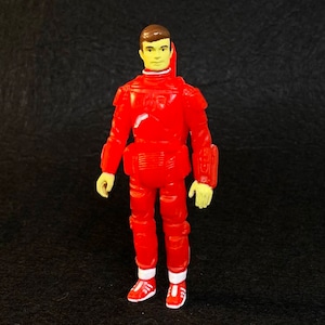 K&ouml;nnte beinhalten: Eine rote Plastik-Actionfigur einer Person, die einen roten Raumanzug mit gelbem Gesicht und braunen Haaren tr&auml;gt. Die Figur steht mit den Armen an den Seiten und tr&auml;gt rote Schuhe mit wei&szlig;en Akzenten.