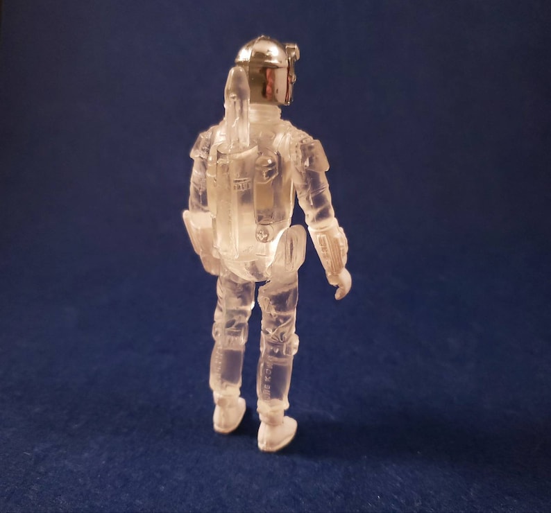 K&ouml;nnte beinhalten: Eine durchsichtige Plastik-Actionfigur von Boba Fett aus Star Wars. Die Figur tr&auml;gt einen Helm und hat einen Jetpack auf dem R&uuml;cken.