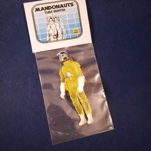 May include: A yellow translucent action figure of a Mandalorian with a white helmet and white armor. The figure is packaged in a clear plastic bag with a white card that reads "Mandonaunts Time Hunter" and "Toy Biz".