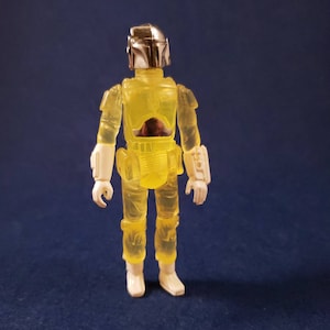 May include: A yellow translucent action figure of a Star Wars character wearing a helmet and armor. The figure has white boots and is standing on a blue background.