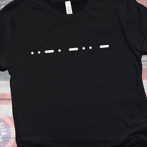 May include: Black t-shirt with a white design of a series of dots and dashes.