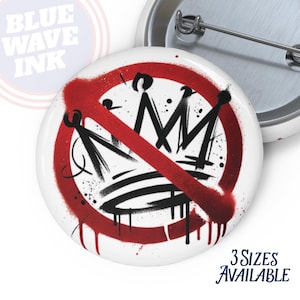 May include: White button with a black and red graphic of a crown crossed out with a red line. The button has a silver pin back. The text "3 Sizes Available" is in the bottom right corner. The text "BLUE WAVE INK" is in the top left corner.