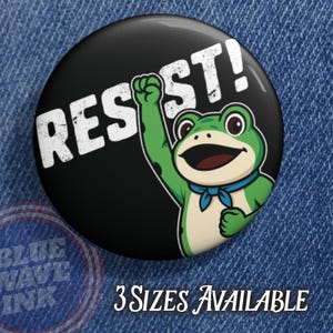 May include: A round black button with the word "RESIST!" in white block letters. A green cartoon frog with a blue neckerchief is raising its fist. The text "3 SIZES AVAILABLE" is below the button.