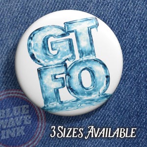 May include: A white button with the blue text "GTFO" in a stylized, icy font. The button is set against a denim background. The text "3 SIZES AVAILABLE" is also visible.