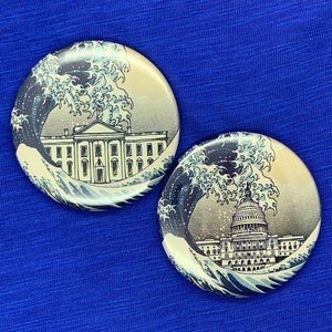 May include: Two round, white and blue ceramic coasters with a graphic of a large wave crashing over the White House and the US Capitol Building.
