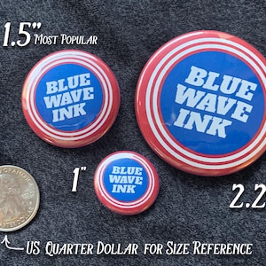 Puede incluir: Tres botones redondos con el texto "BLUE WAVE INK" en blanco sobre fondo azul, rodeados de anillos rojos y blancos. Los tama&ntilde;os son 2,54 cm, 3,81 cm y 5,69 cm de di&aacute;metro. Se incluye un cuarto de d&oacute;lar estadounidense como referencia de tama&ntilde;o.