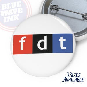 May include: White button with the letters "fdt" in a red, black, and blue color block design. The text "3 Sizes Available" is below the button. The logo "Blue Wave Ink" is in the upper left corner.