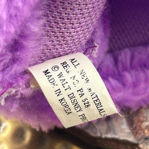 May include: Close-up of a plush toy with purple fur and a tag. The tag reads "ALL NEW MATERIALS, REG. NO. PA 528, &copy; WALT DISNEY PRO, MADE IN KOREA."