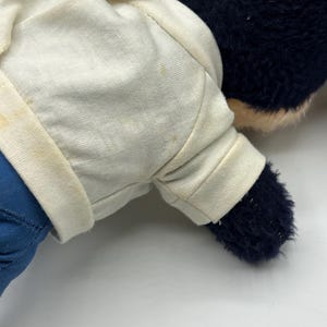 Peut inclure: Un ours en peluche vintage avec une chemise blanche et un pantalon bleu. L'ours a une fourrure bleu fonc&eacute; et un museau beige clair. La chemise a une fermeture &agrave; bouton et les bras et les jambes de l'ours sont visibles.