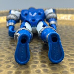 K&ouml;nnte beinhalten: Eine blaue und silberne Actionfigur mit beweglichen Gliedma&szlig;en. Die Figur hat ein V-f&ouml;rmiges Brustdesign und silberne Akzente an Armen und Beinen. Die F&uuml;&szlig;e haben eine einzigartige Form mit dem Text "BANDAI 2007 MADE IN CHINA".