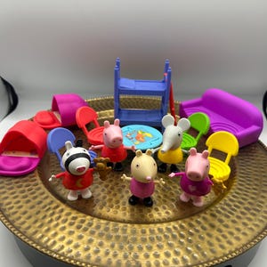 May include: A collection of Peppa Pig plastic toy figures including a zebra, two pigs, and an elephant, accompanied by miniature furniture pieces such as a purple sofa, blue bunk bed, colourful chairs, and a small round table with a printed surface.