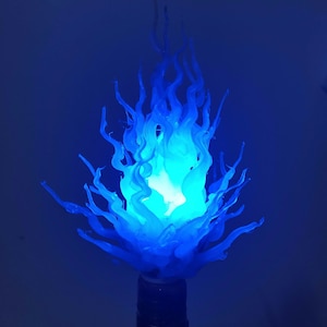 May include: A blue flame-shaped lamp with a light source at its centre. The lamp has a base and is designed to resemble a stylized flame. The colour is a vibrant blue, creating a striking visual effect. The lamp is suitable for home decor.