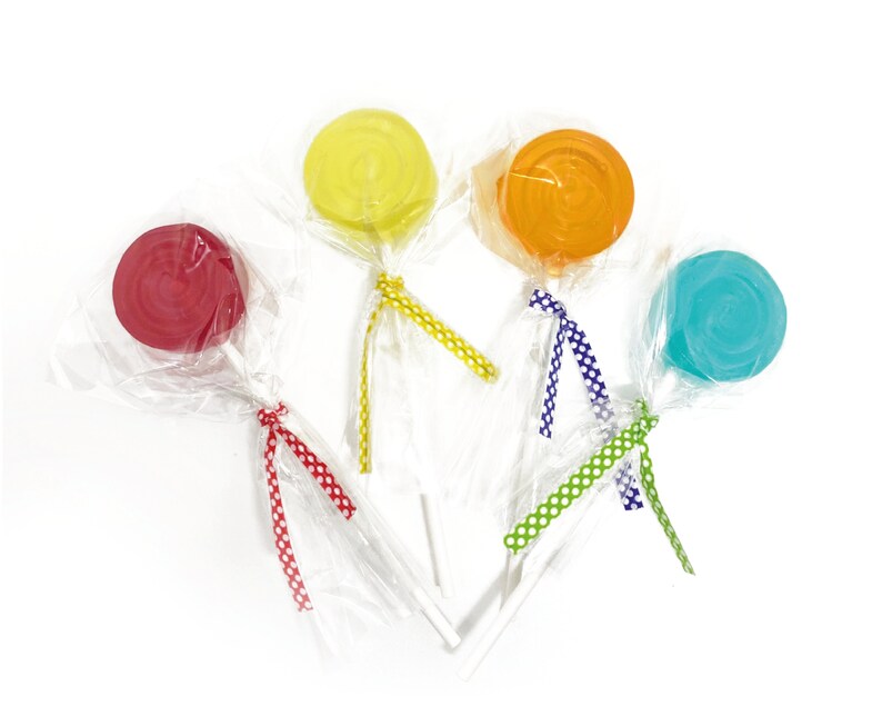 May include: Five colorful lollipops wrapped in clear plastic with polka dot ribbon ties. The lollipops are red, yellow, orange, blue, and green.