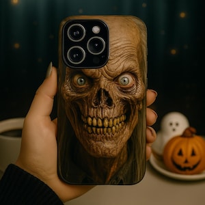 May include: A phone case featuring a detailed, close-up image of a zombie face with blue eyes and a wide grin. The case has a dark background and is held in a hand. The theme is Halloween.