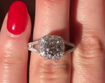 May include: A silver-coloured ring featuring a large, cushion-cut centre stone surrounded by a halo of smaller round stones. The band is split into two sections, each encrusted with tiny pavé stones. The text HARVIN JEWELS is printed below the ring.