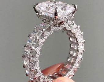 May include: A silver-toned ring featuring a large, rectangular, faceted clear stone set in a prong setting. The band is fully encrusted with smaller, square-cut clear stones arranged in a continuous eternity style, creating a highly reflective surface.
