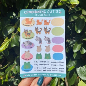 May include: A sticker sheet with a variety of cute animal illustrations. The sheet includes cats, dogs, opossums, frogs, and the text "Concerning Cuties Sticker Sheet".