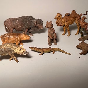 Peut inclure: Une collection de figurines d'animaux vintage, comprenant un bison, un chameau, un ours, un hippopotame, une hyène, un alligator et une figurine d'un Amérindien. Les figurines sont en métal peint et ont un aspect rustique et antique.