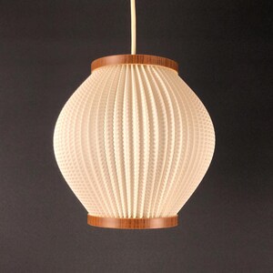 May include: Cream-coloured pendant light with a textured, ribbed shade and wooden trim. The light fixture hangs from a thin, off-white cord. The shade has a rounded shape, and the wooden trim is a warm brown colour.