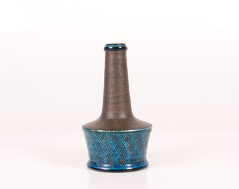May include: A brown ceramic vase with a blue geometric pattern around the base. The vase has a narrow neck and a wide base.