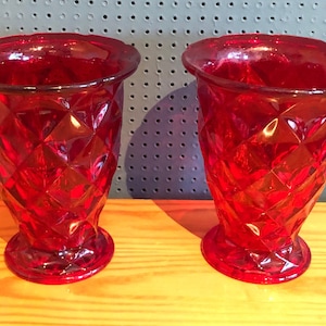 Könnte beinhalten: Zwei rote Glasvasen mit einem Diamantenmuster. Die Vasen stehen auf einer Holzoberfläche.