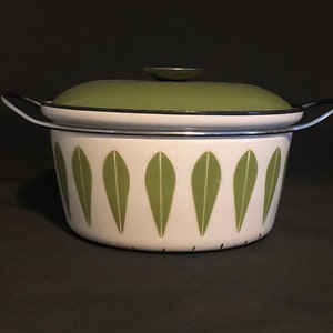 Può includere: Una pentola vintage in smalto bianco con coperchio e manici verdi. La pentola presenta un motivo ripetuto di forme di foglie verdi. Il coperchio ha una piccola maniglia rotonda. La pentola è progettata per cucinare.