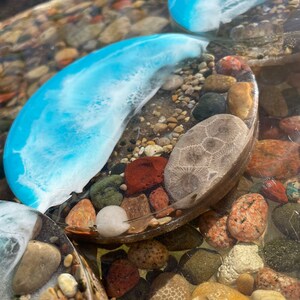 May include: Two round blue resin coasters with white swirls and embedded stones, including a fossilized sea urchin, on a bed of small stones.