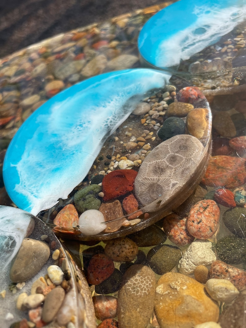 May include: Two round blue resin coasters with white swirls and embedded stones, including a fossilized sea urchin, on a bed of small stones.