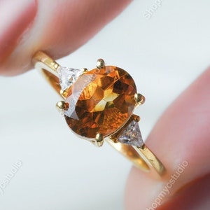 May include: A gold ring with a large oval-shaped orange gemstone and two smaller triangular clear gemstones.