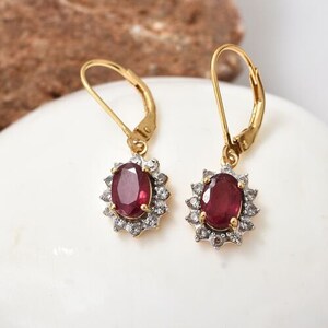 May include: A pair of gold earrings with a red oval gemstone surrounded by smaller white gemstones.