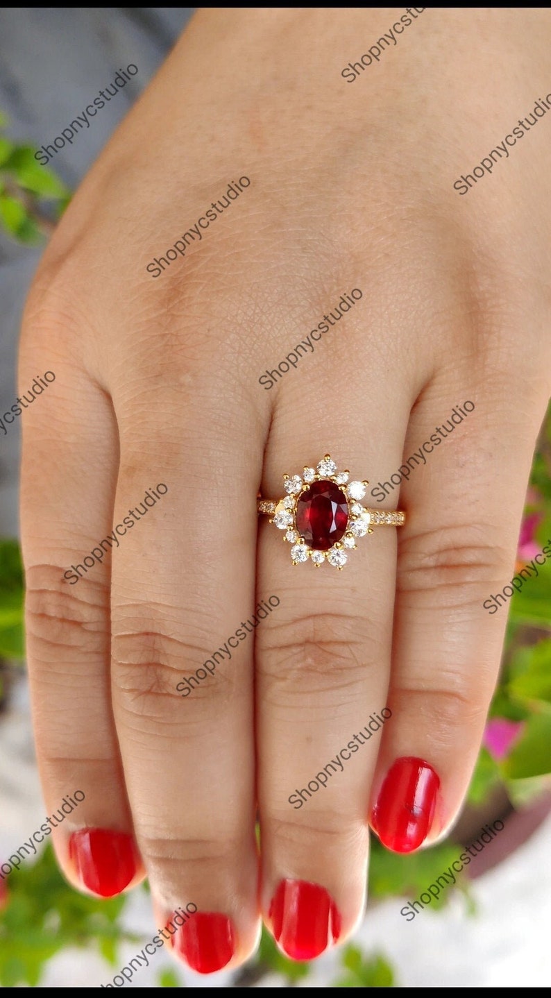 May include: A gold ring with a large oval red gemstone surrounded by smaller white gemstones.