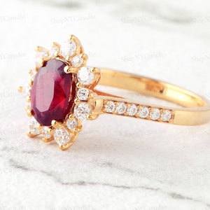 May include: A gold ring with a large oval red gemstone surrounded by smaller clear gemstones. The band is also set with clear gemstones.