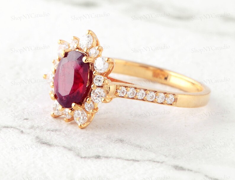 May include: A gold ring with a large oval red gemstone surrounded by smaller clear gemstones. The band is also set with clear gemstones.