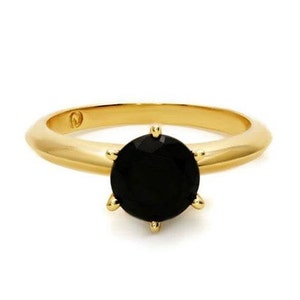May include: A gold ring with a black gemstone set in a prong setting.