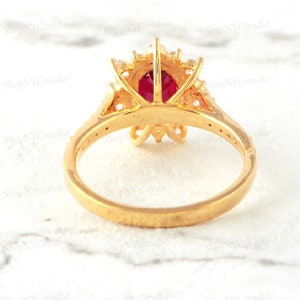 May include: A gold ring with a large red gemstone surrounded by smaller white gemstones. The ring is set in a floral design.