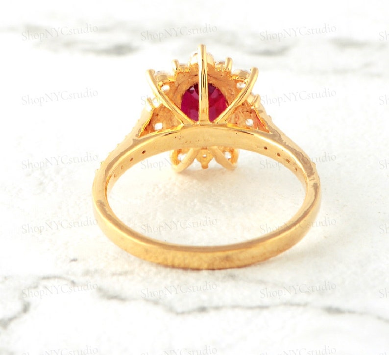May include: A gold ring with a large red gemstone surrounded by smaller white gemstones. The ring is set in a floral design.