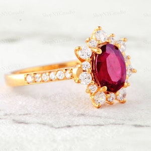 May include: A gold ring with a large oval ruby surrounded by smaller diamonds. The ring is set in a floral design.