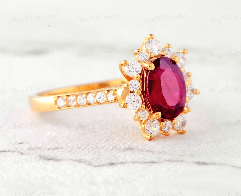 May include: A gold ring with a large oval ruby surrounded by smaller diamonds. The ring is set in a floral design.