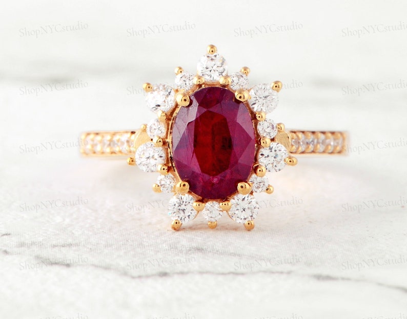 May include: A gold ring with a large oval ruby surrounded by a halo of smaller diamonds. The ring is set on a white background.