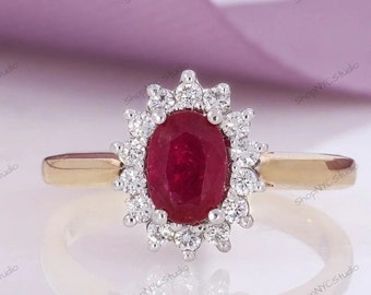 Può includere: Un anello in oro con una pietra preziosa ovale di rubino rosso circondata da un alone di piccoli diamanti rotondi.