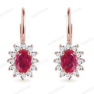 May include: A pair of rose gold leverback earrings. Each earring has an oval ruby centre, encircled by small, round, white diamonds. The earrings have a floral design and are set against a white background.
